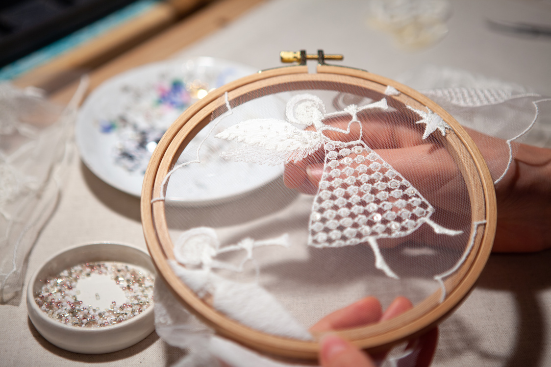 Workplace of an embroiderer with embroidery frames, angel embroidery, beads. The embroiderer's hands hold the embroidery hoop